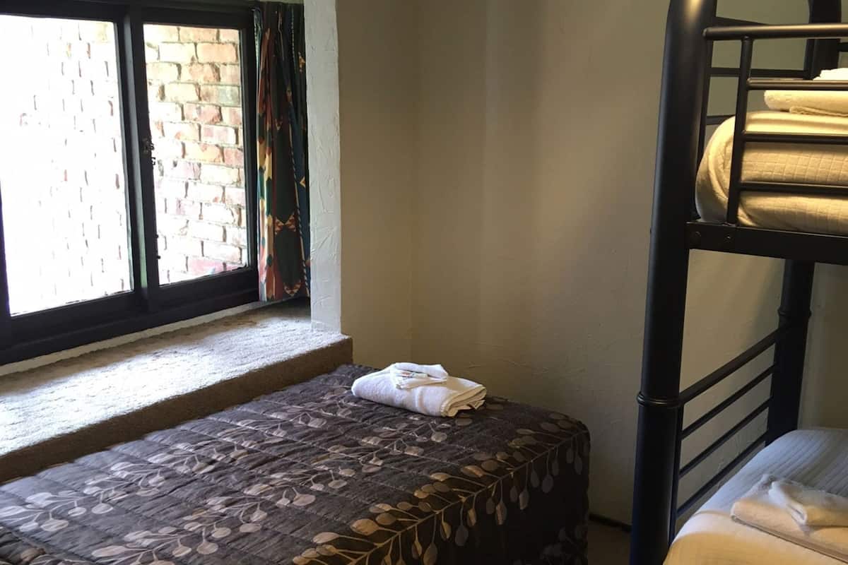 A bunk bed room with a window, a small bench, and a bed with a leaf-patterned bedspread.