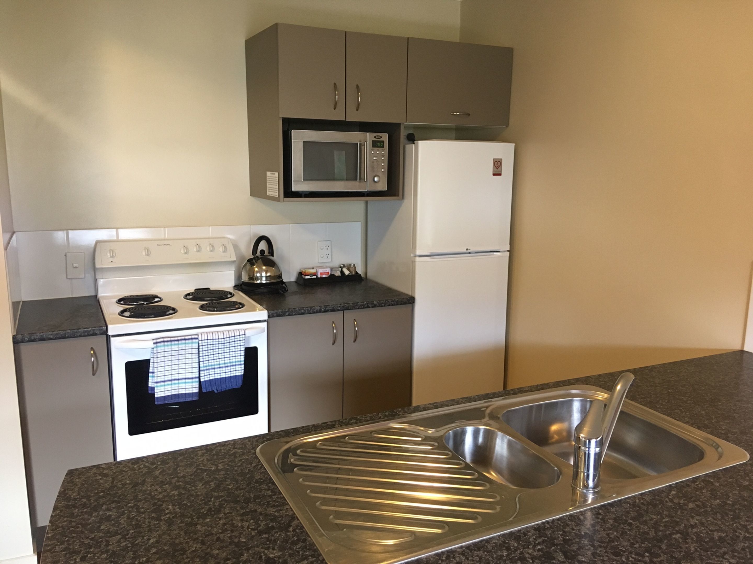 A kitchen with a stove, microwave, refrigerator, and a stainless steel sink.