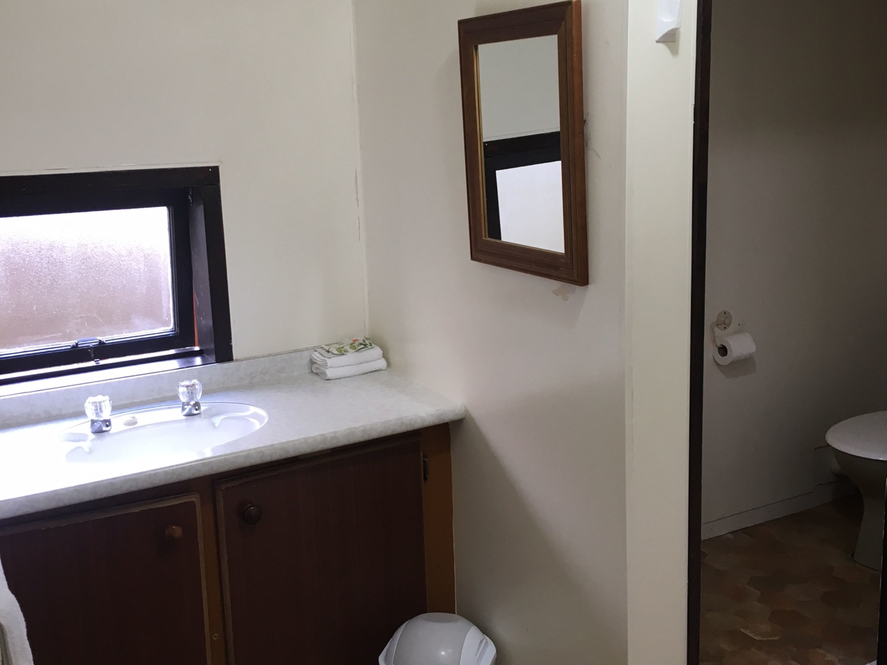 A bathroom with a sink, mirror, toilet, and a window.