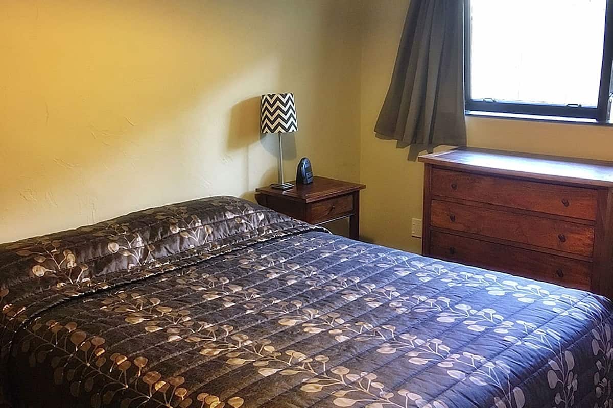 A bedroom with a bed, a nightstand, a dresser, and a window with curtains.
