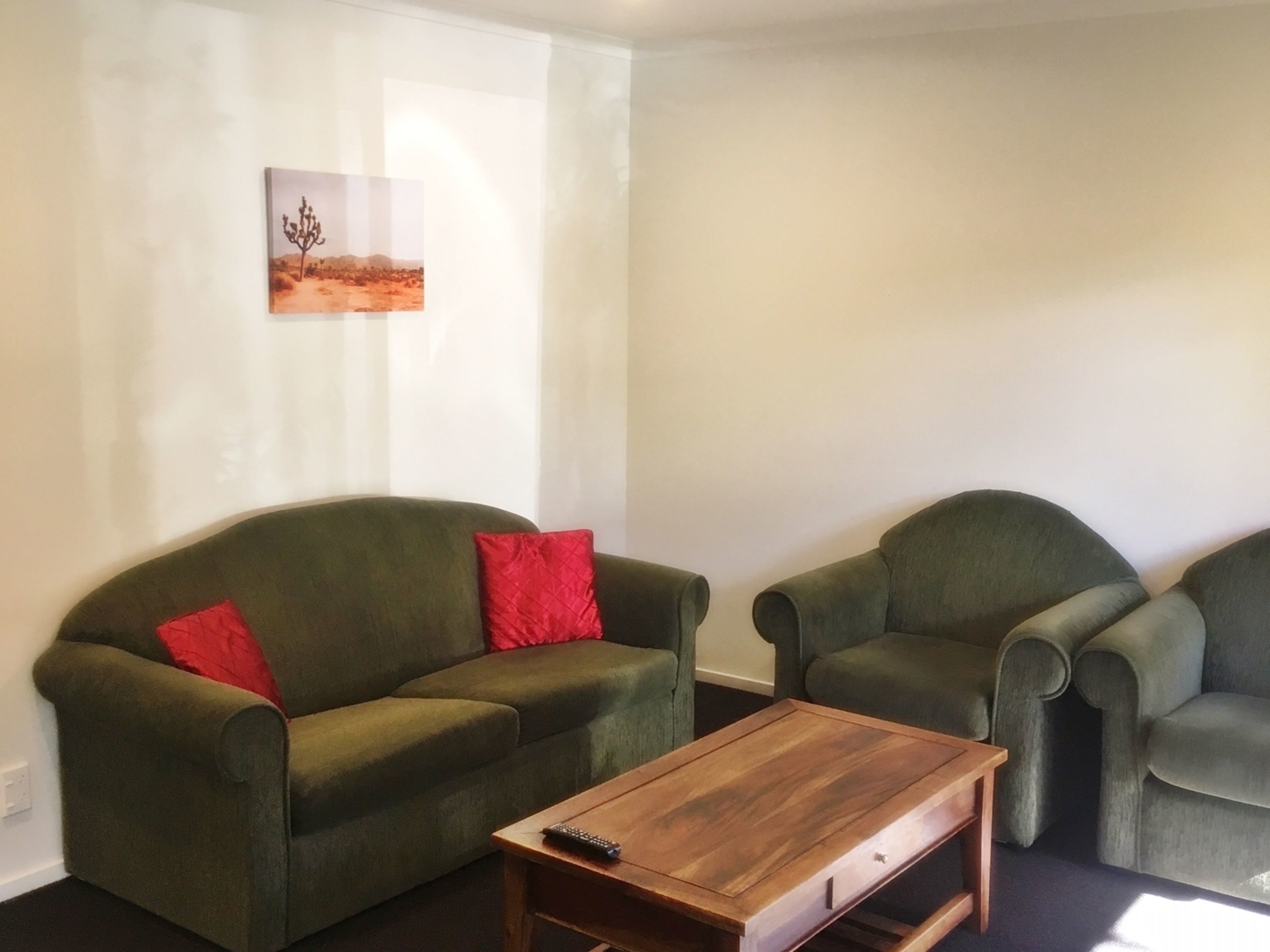 A living room with a green sofa, a wooden coffee table, and a painting of a desert landscape.
