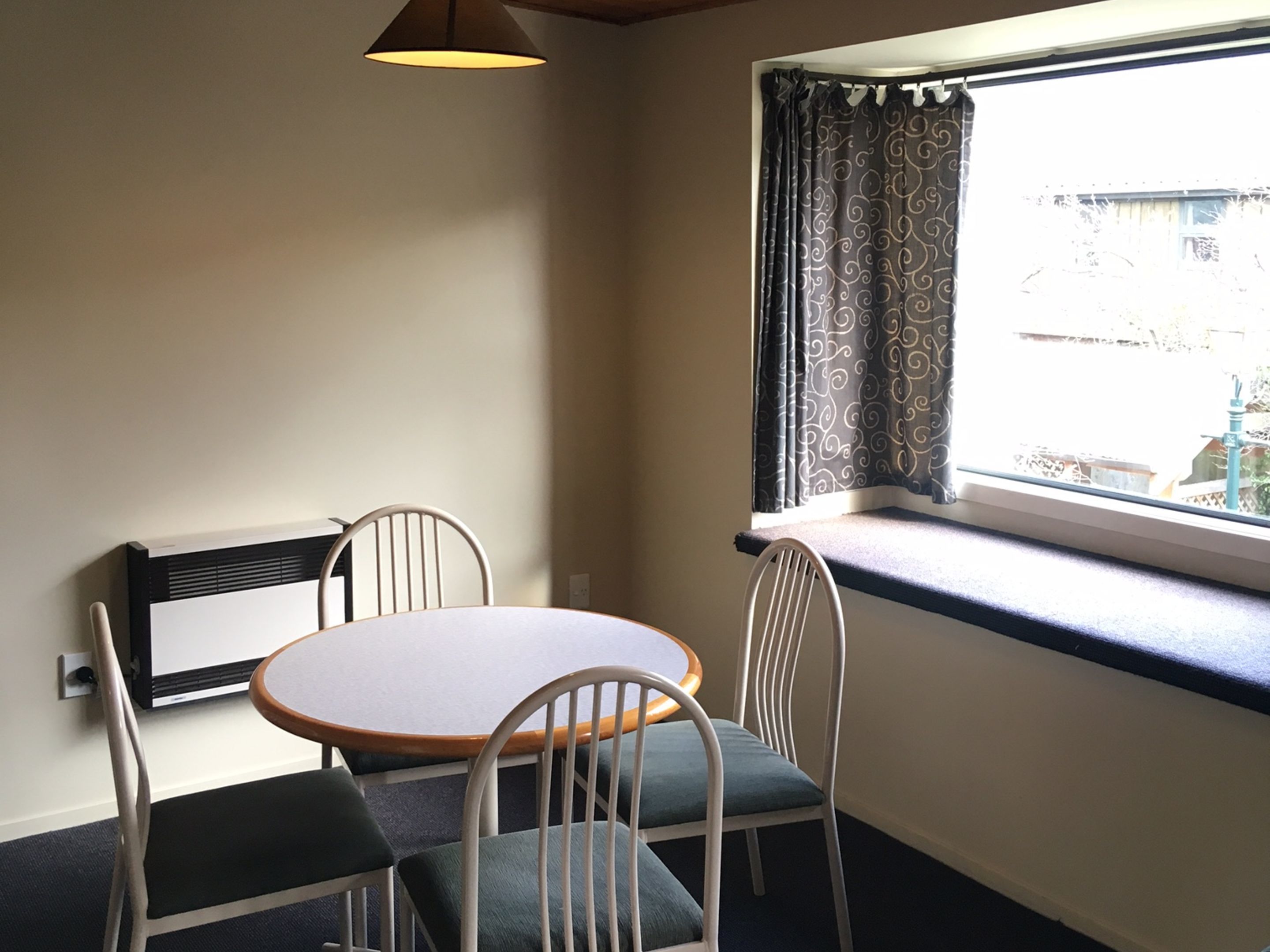 Ein kleiner Essbereich mit einem runden Tisch, vier Stühlen, einem Fenster mit Vorhängen und einem Wandheizgerät.