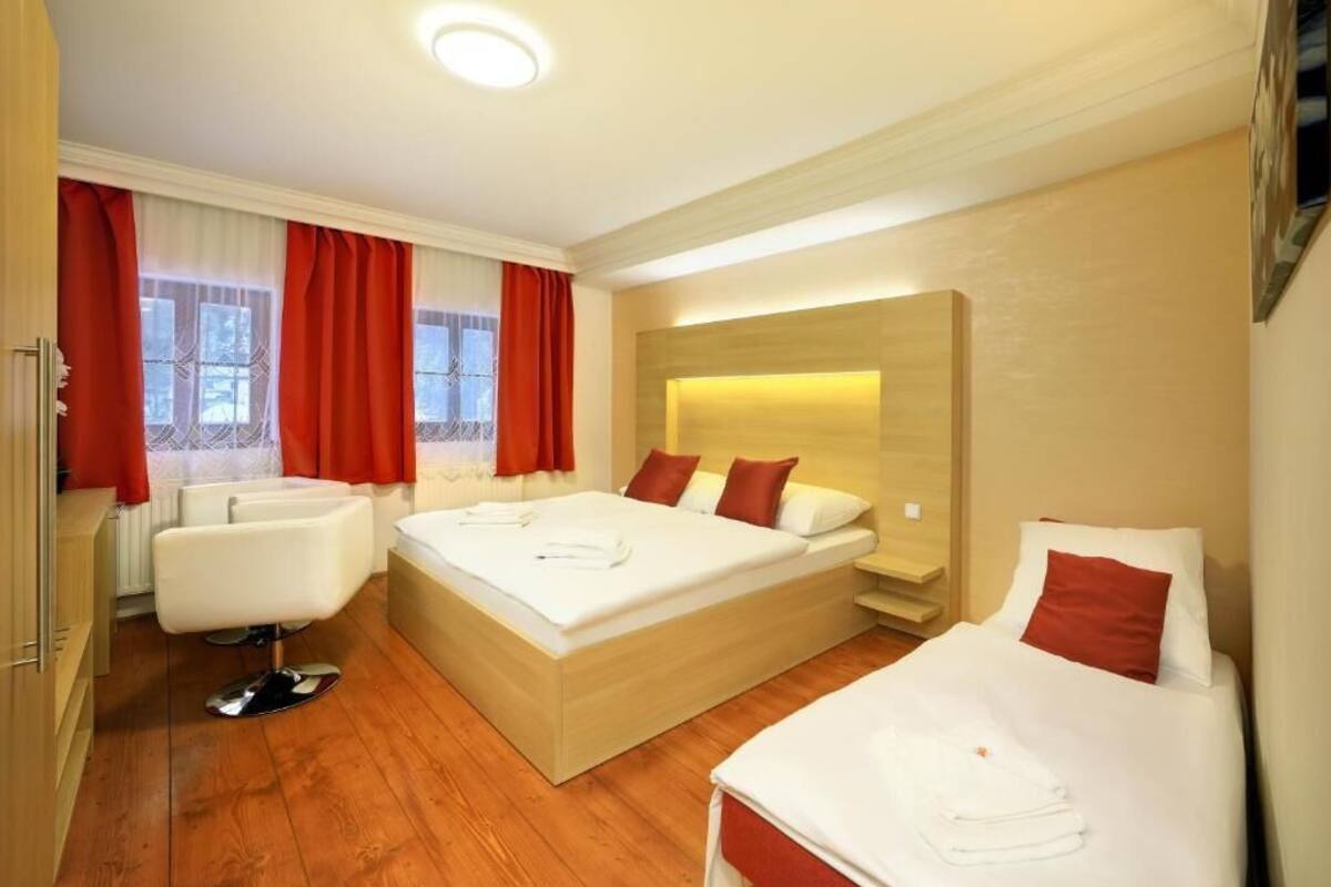 Habitación de hotel con dos camas, un área de descanso y un ventanal grande con cortinas.