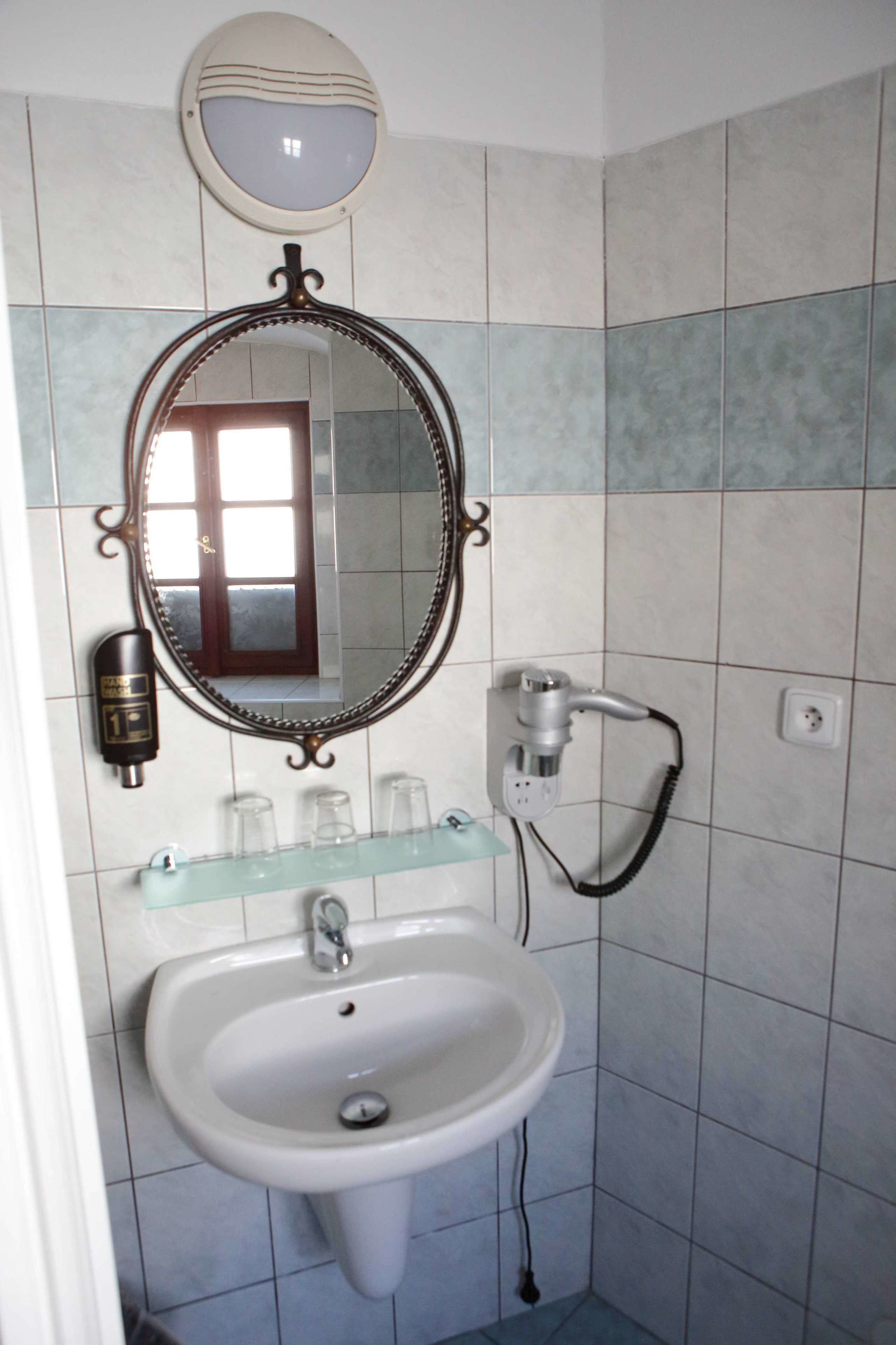A bathroom with a white sink, a mirror, and a hairdryer on a wall-mounted shelf.