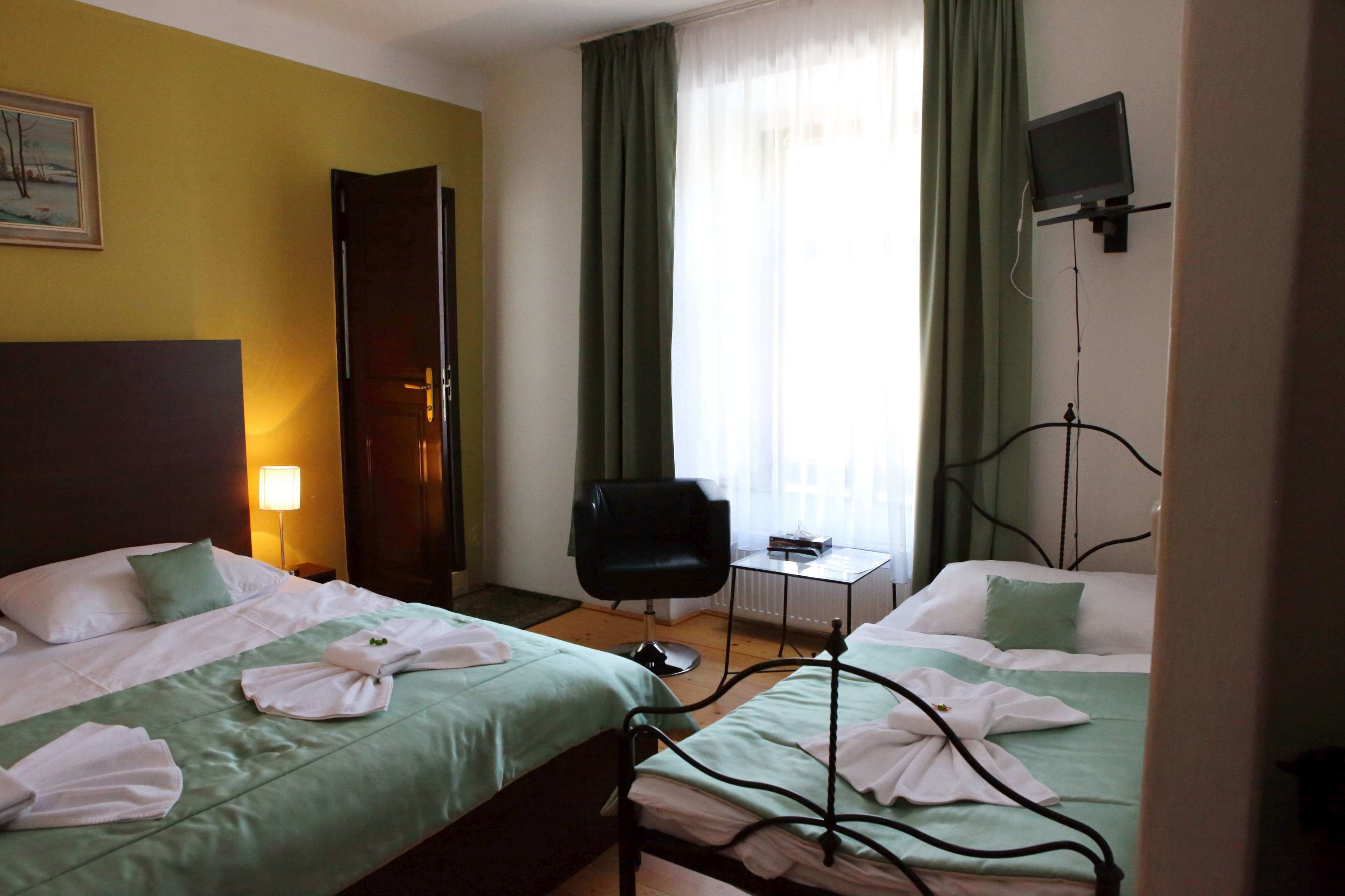 A hotel room with two beds, a chair, a small table, a TV, and a painting on the wall.