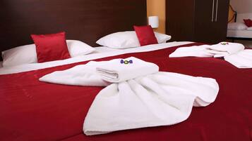 Ett hotellrum med en stor säng, röda sängkläder, vita kuddar och prydligt hopvikta handdukar på sängen.