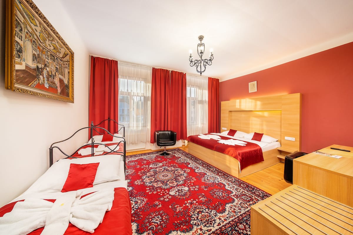Una habitación de hotel con dos camas, un cuadro grande, una araña y una alfombra roja.