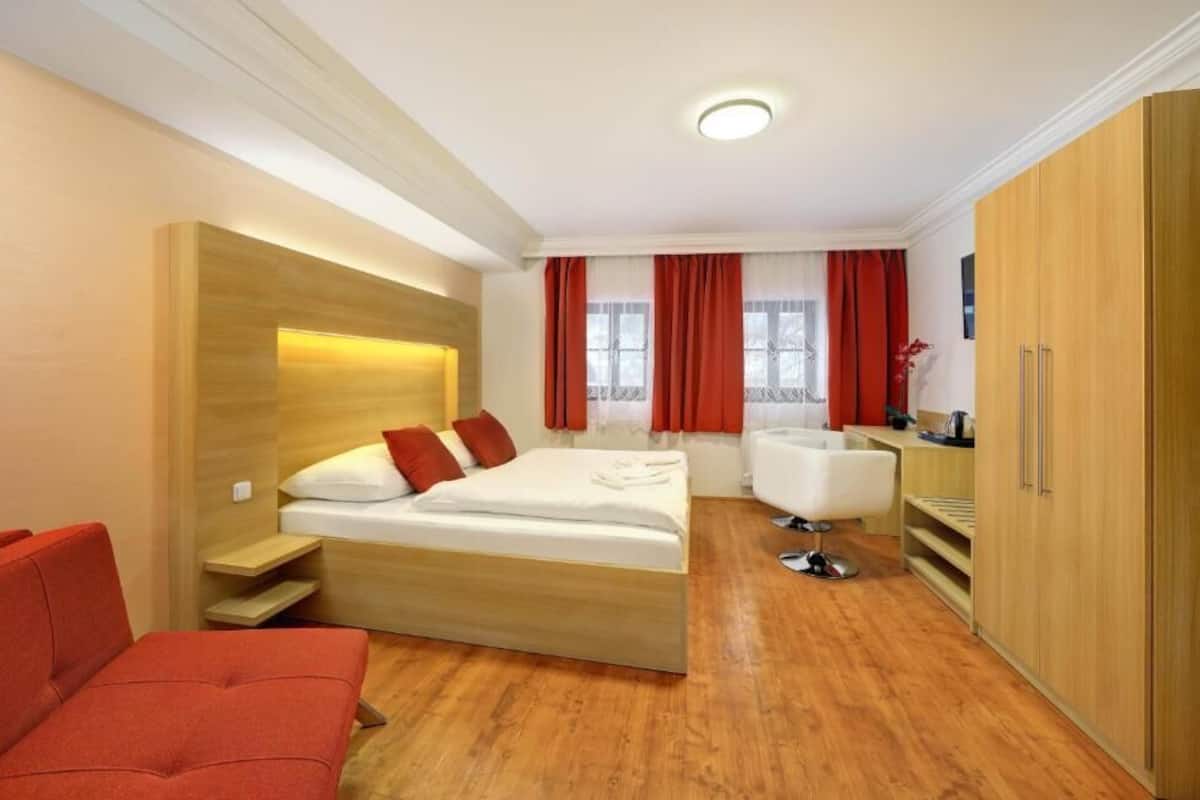 Una habitación de hotel moderna con una cama de madera, un sofá rojo, un escritorio y un armario.