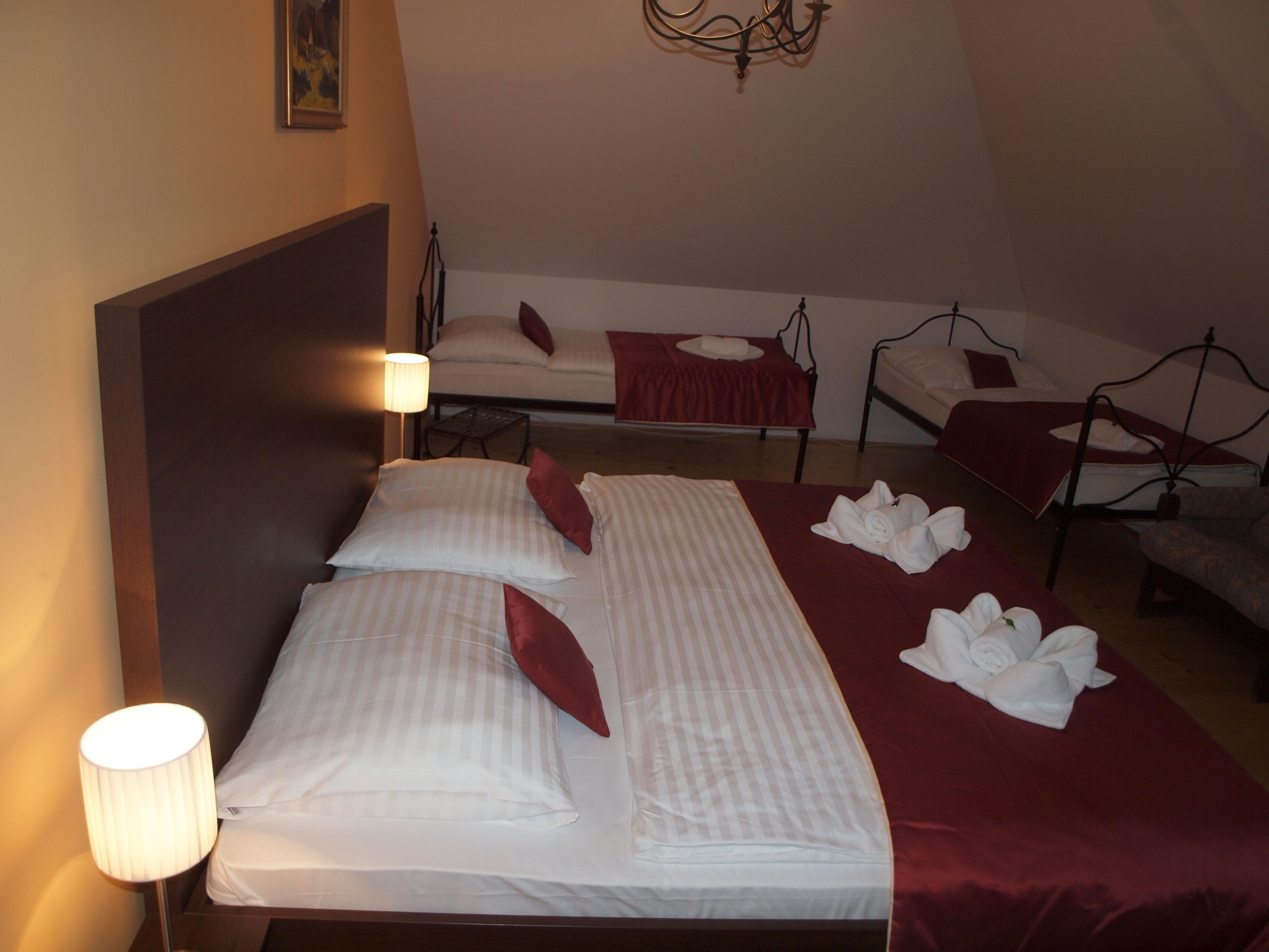 A hotel room with a large bed, two smaller beds, a desk, and a lamp.