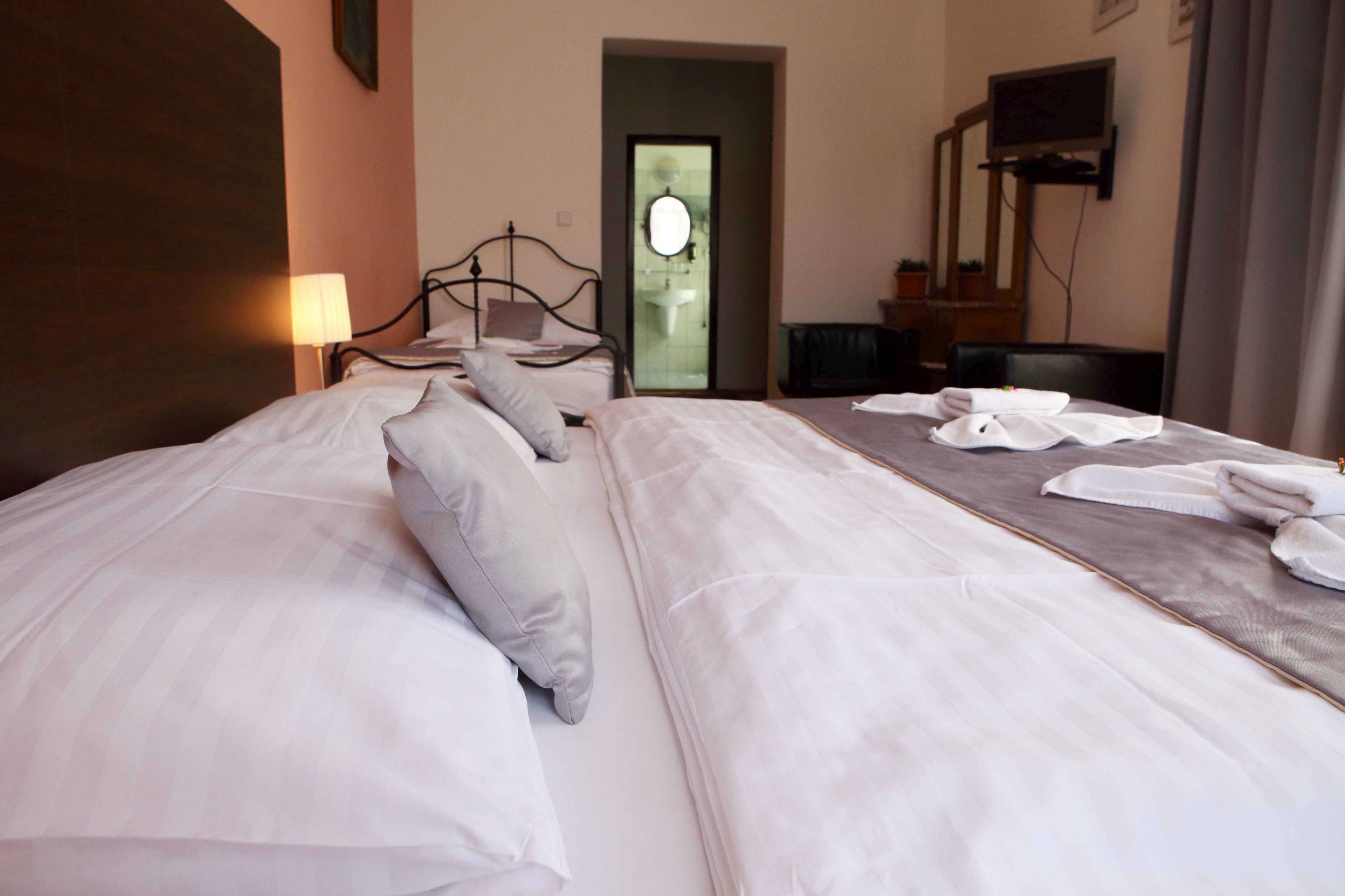 A hotel room with a large bed, a bedside table, a lamp, a TV, and a bathroom door.