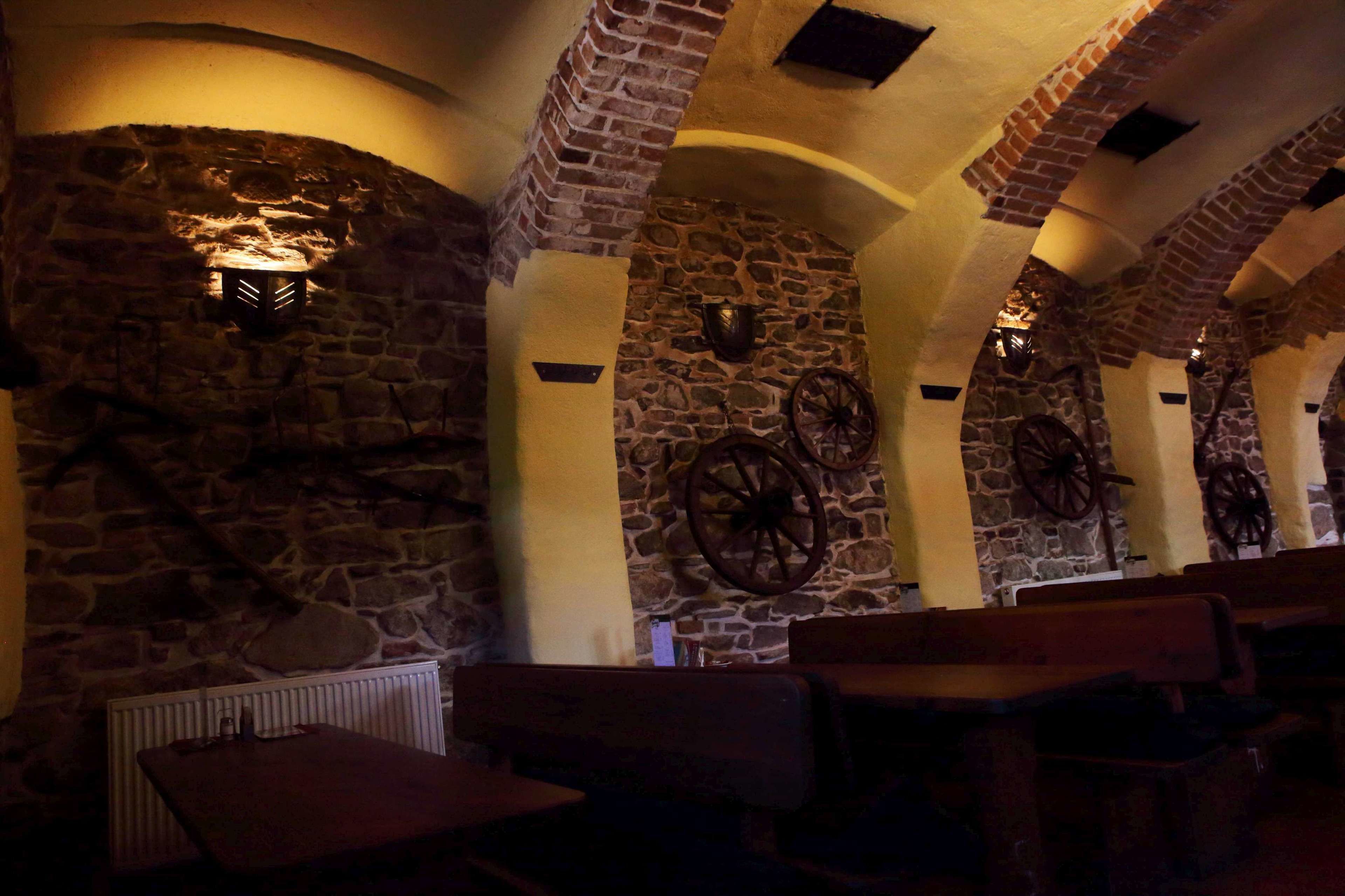 A stone-walled interior with wooden benches and a fireplace.