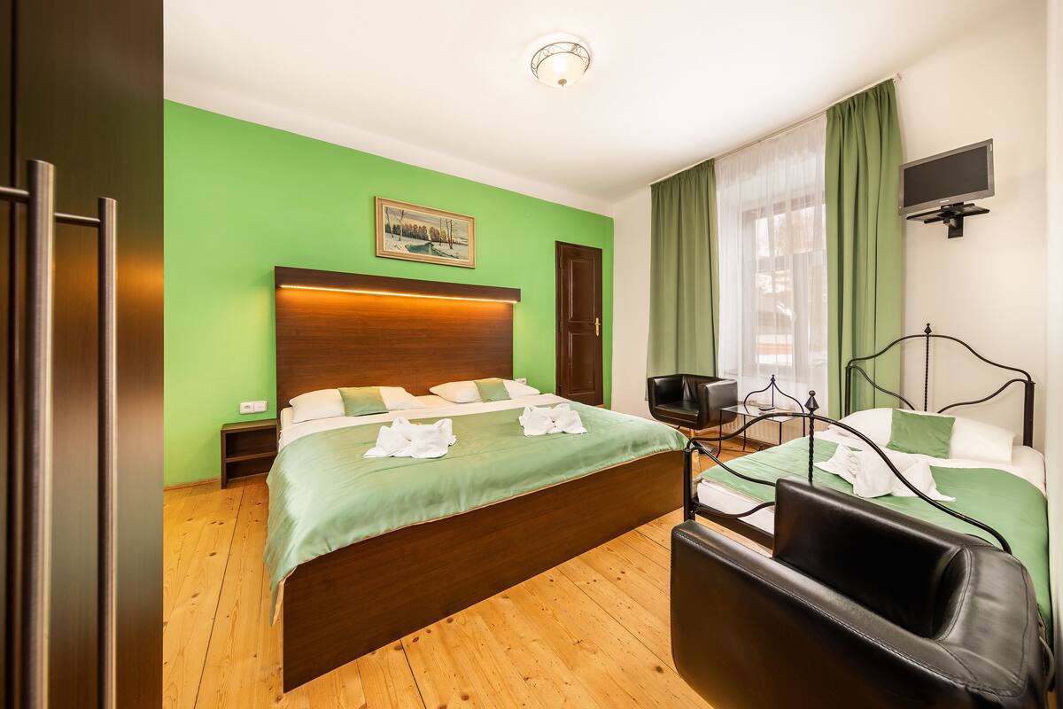 Una habitación de hotel con una cama grande, un escritorio, una silla, un televisor y una pared verde.
