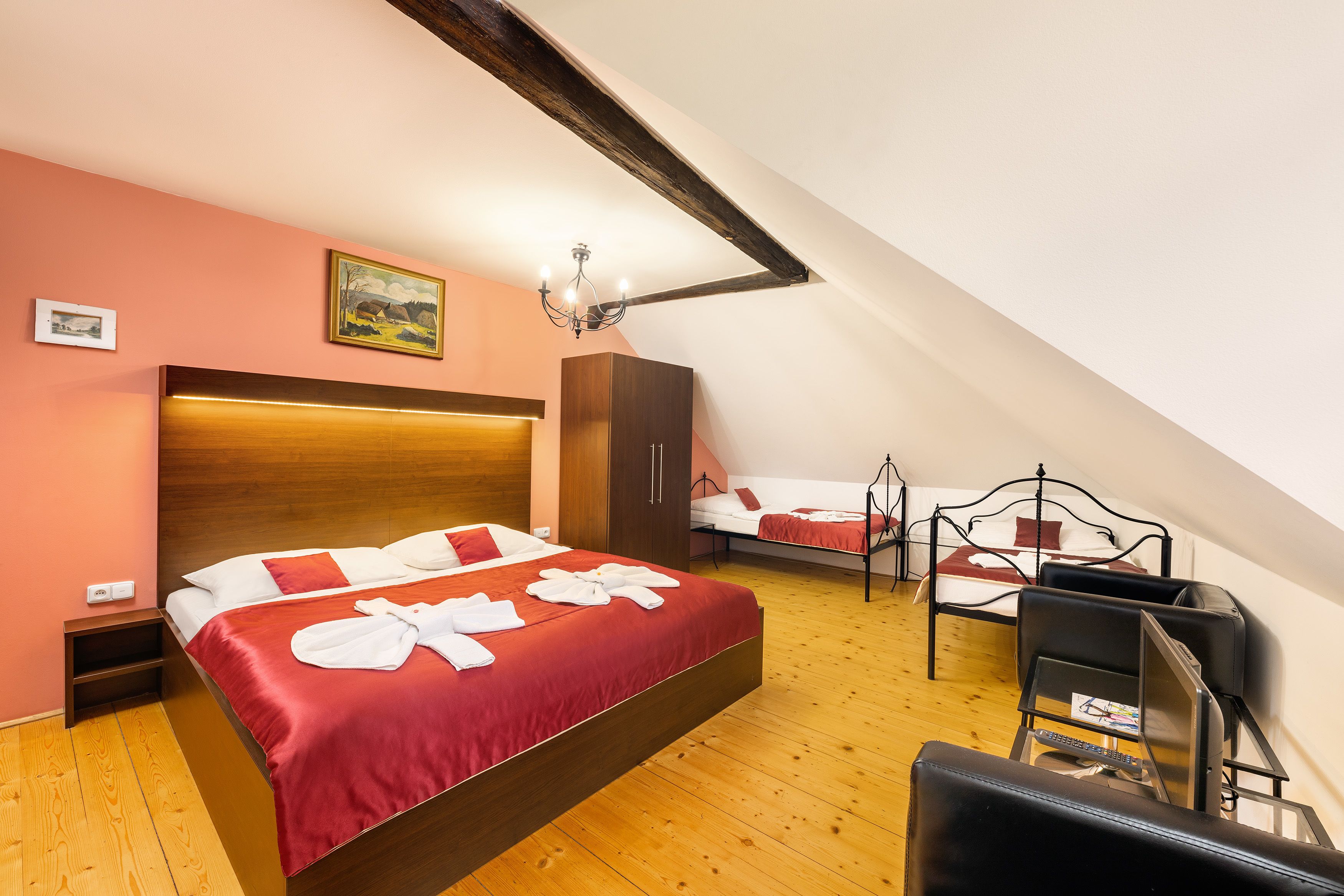 A bedroom with a large bed, a smaller bed, a desk with a chair, a wardrobe, and a painting on the wall.