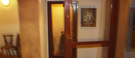 Un pasillo interior con un arco de entrada, una silla de madera y un cuadro en la pared.