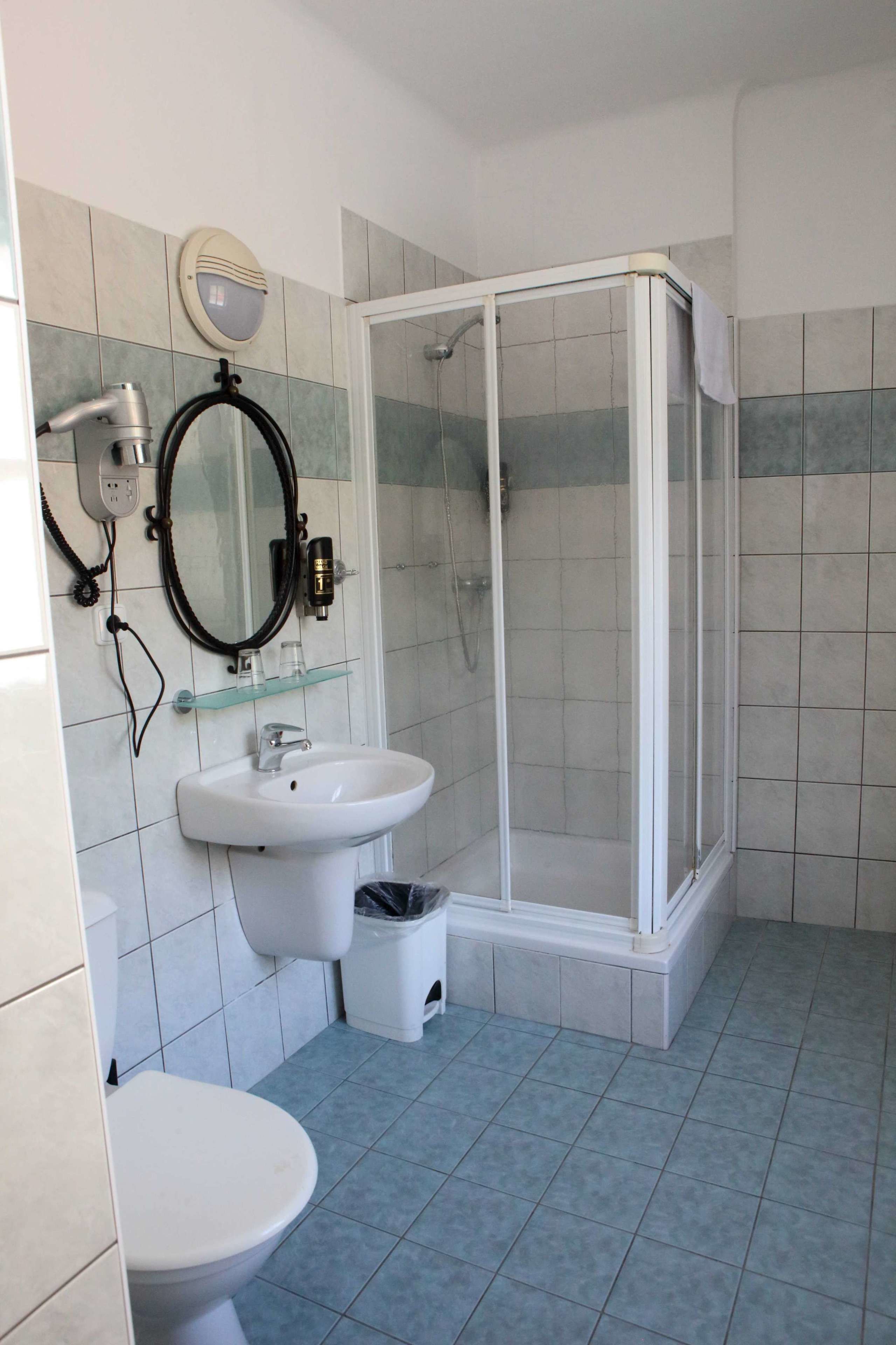 A bathroom with a white sink, mirror, and toilet, a glass shower enclosure, and tiled walls.