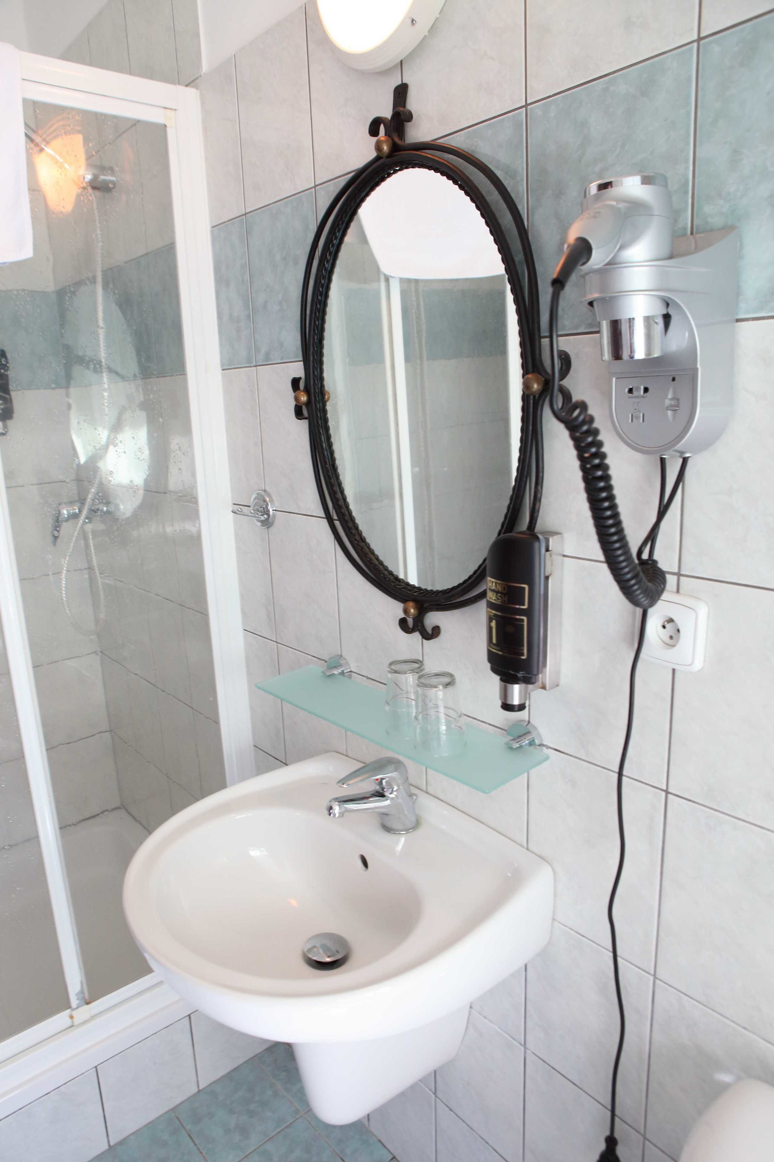 Ein Badezimmer mit Duschkabine aus Glas, einem weißen Waschbecken und einem an der Wand befestigten Föhn.