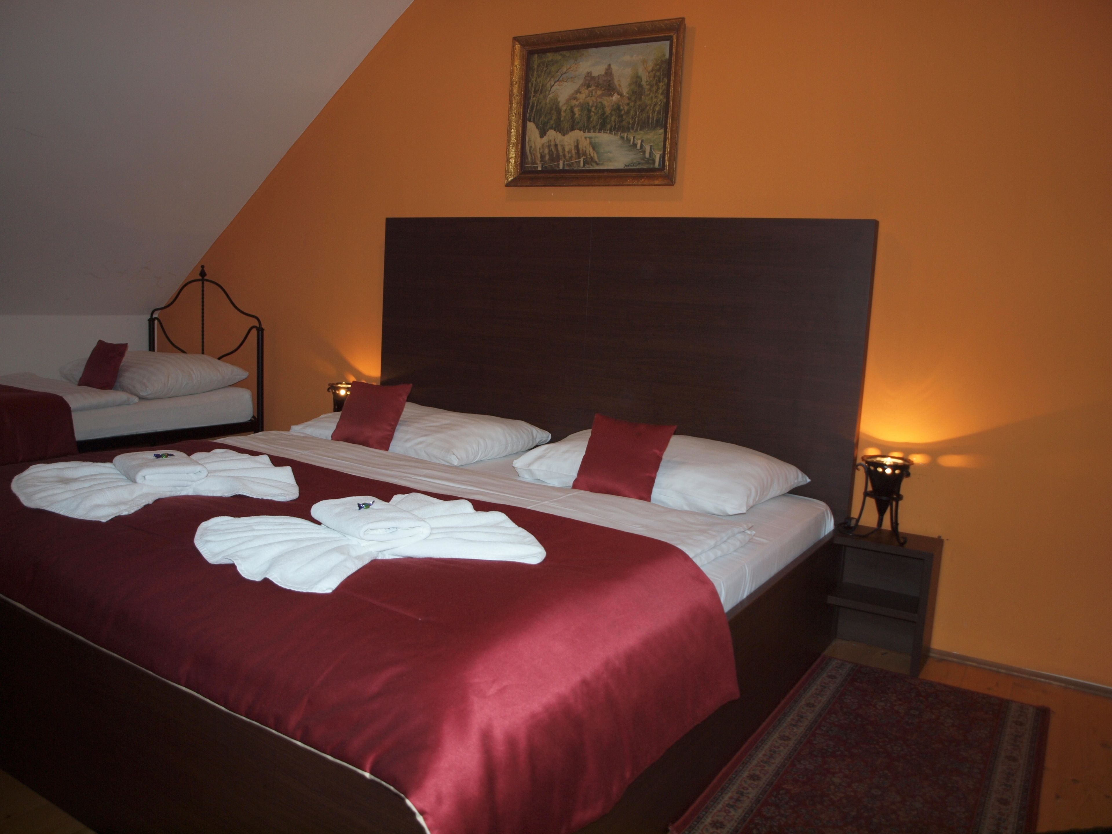 Een hotelkamer met twee bedden, rode beddengoed, een schilderij aan de muur en een nachtkastje met een lamp.