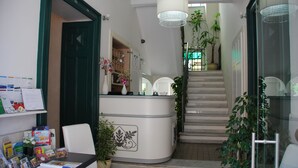 Een receptie met een balie, stoelen, een trap en plantenbakken.