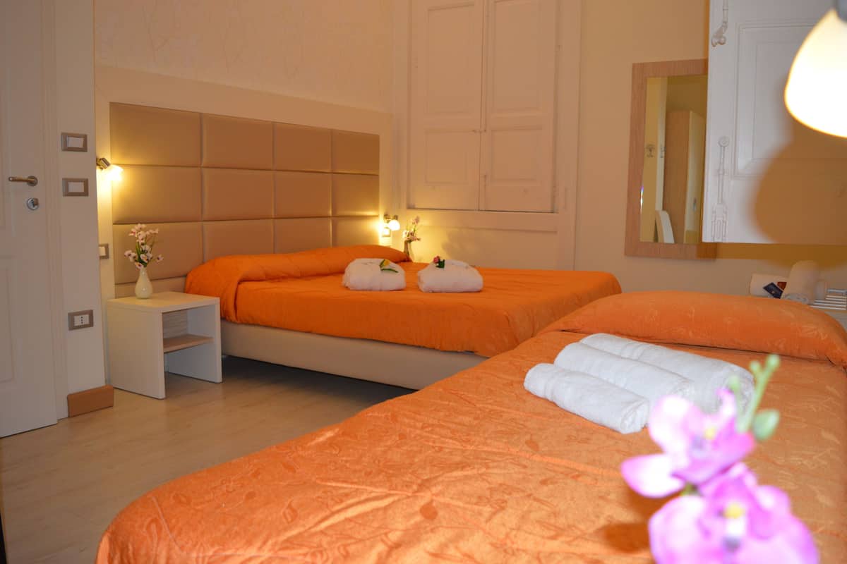 A hotel room with two beds, a bedside table with a vase of flowers, and a mirror on the wall.