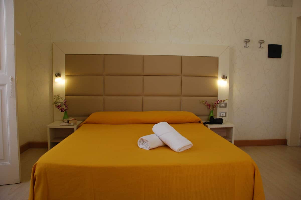 A neatly made bed with a headboard, two bedside tables with lamps, and a vase with flowers on one table.