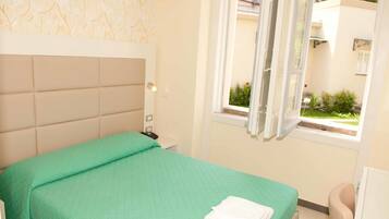 Quarto com colcha verde, cabeceira branca, mesa de cabeceira com telefone e janela com cortinas.