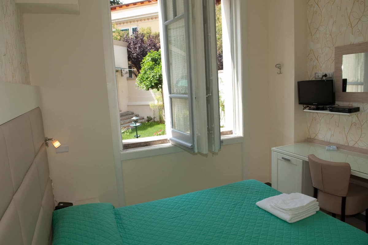 A hotel room with a bed, a desk with a chair, a television, and a window with an open curtain.