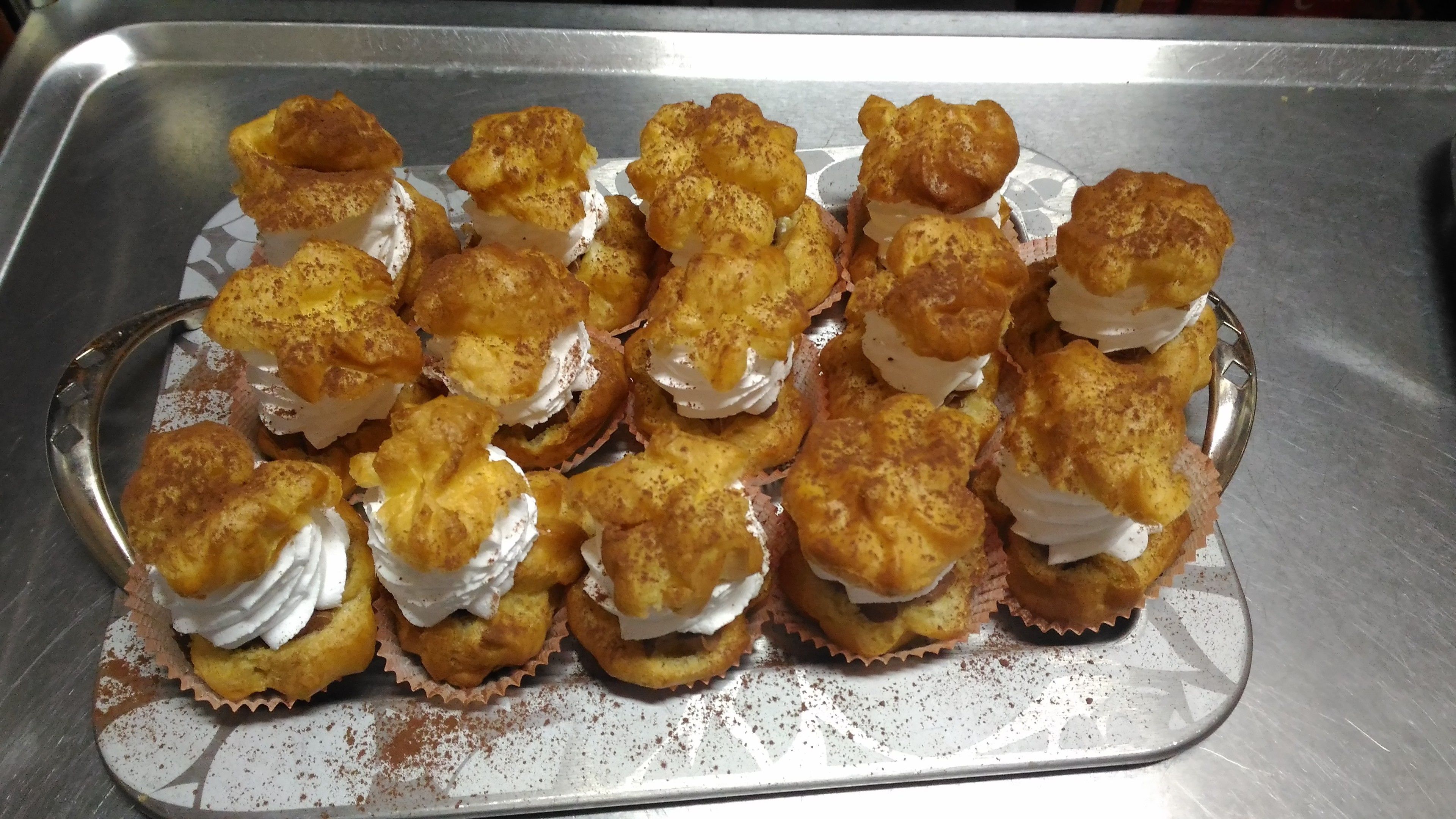 A tray of éclairs with cream on a metal surface.