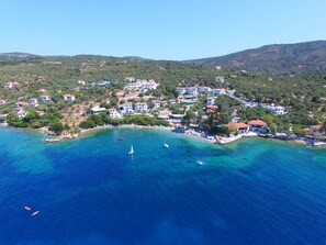 An aerial view of a coastal town with buildings, clear blue waters, and boats. - Leda Village Resort (South Pelion)