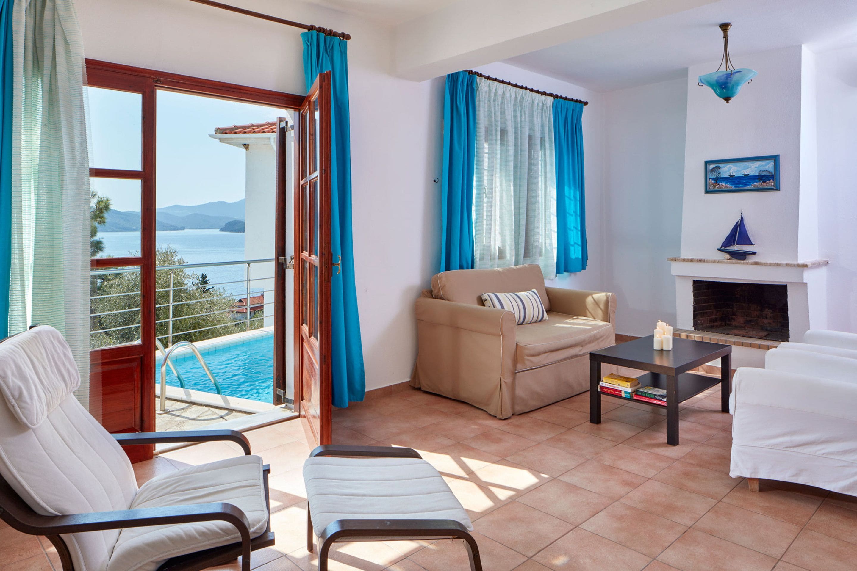 A living room with a view of the sea, a sofa, a chair, a small table, and a fireplace.