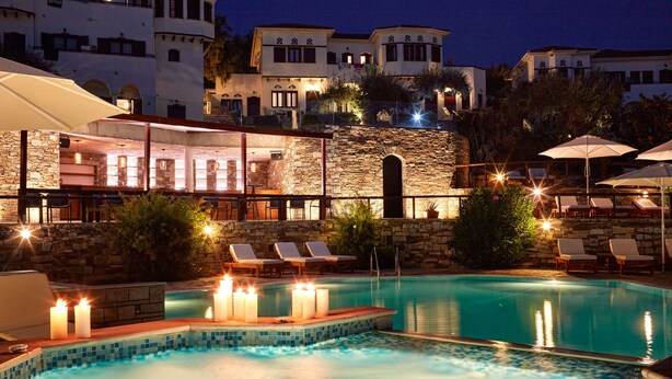 A pool area with lounge chairs and candles, surrounded by stone walls and buildings with arched windows. - Leda Village Resort (South Pelion)