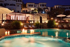 A pool area with lounge chairs and candles, surrounded by stone walls and buildings with arched windows. - Leda Village Resort (South Pelion)