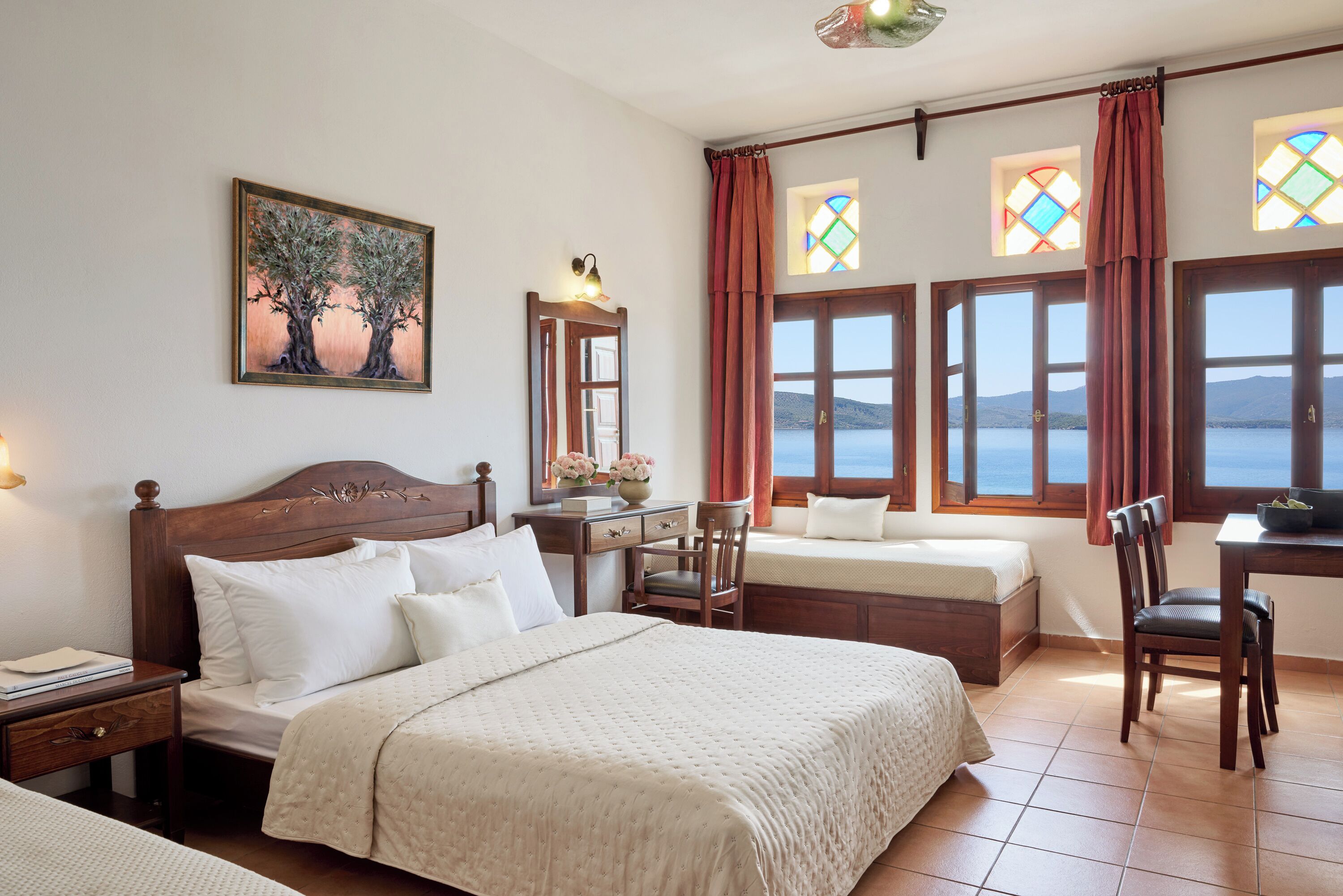 A hotel room with a large bed, a desk, and a chair. There are two windows with curtains, and a painting on the wall.