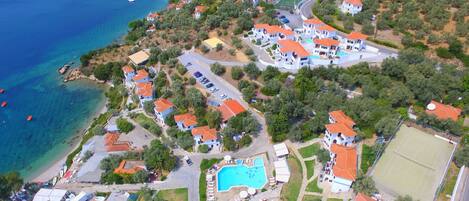 An aerial view of a coastal residential area with houses, a swimming pool, and a tennis court.