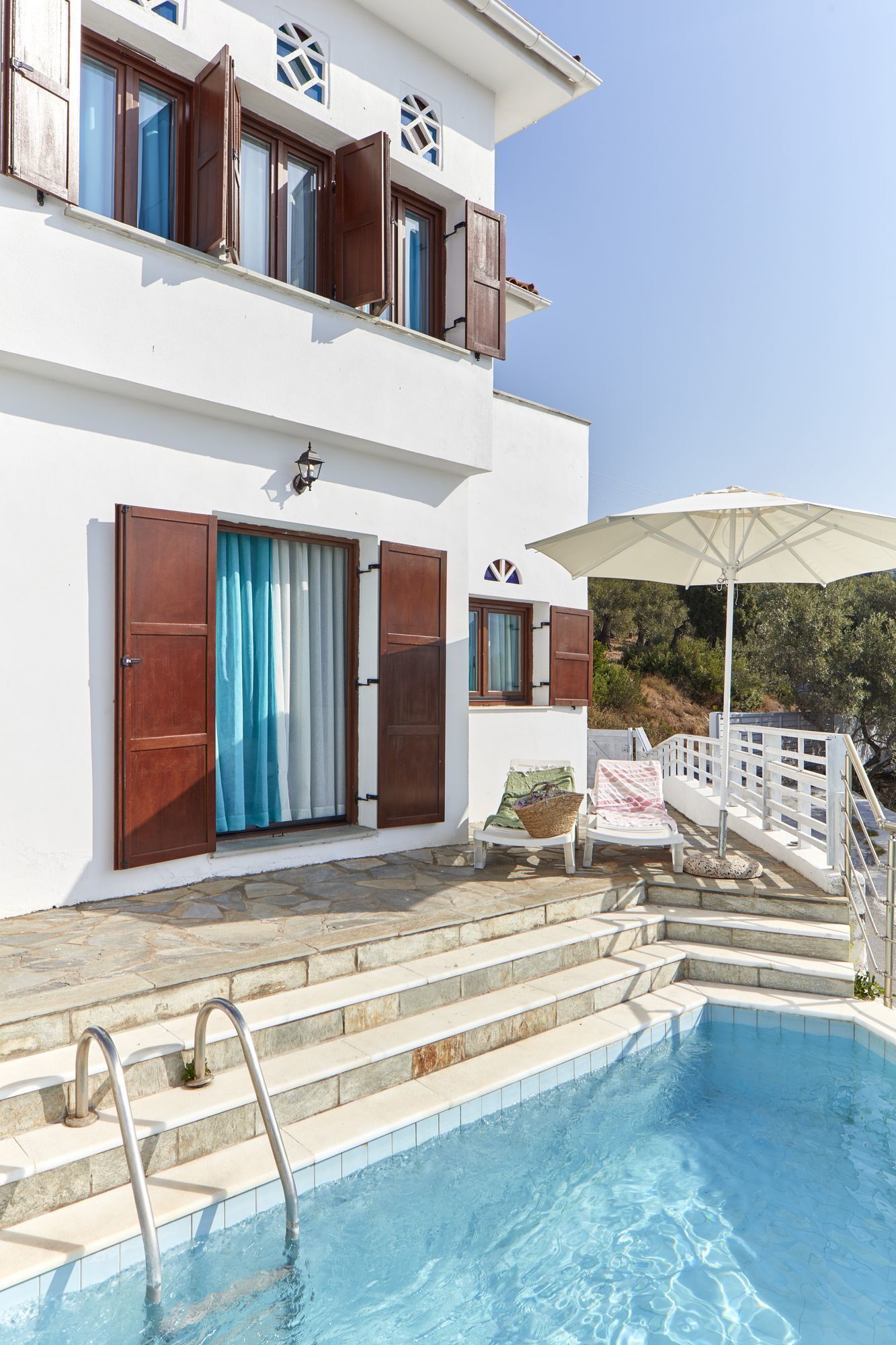 A two-story building with a swimming pool, outdoor seating, and a white fence.