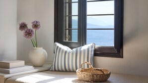 A room with a window, a vase with flowers, striped pillows, a basket, and a stack of books. - Leda Village Resort (South Pelion)