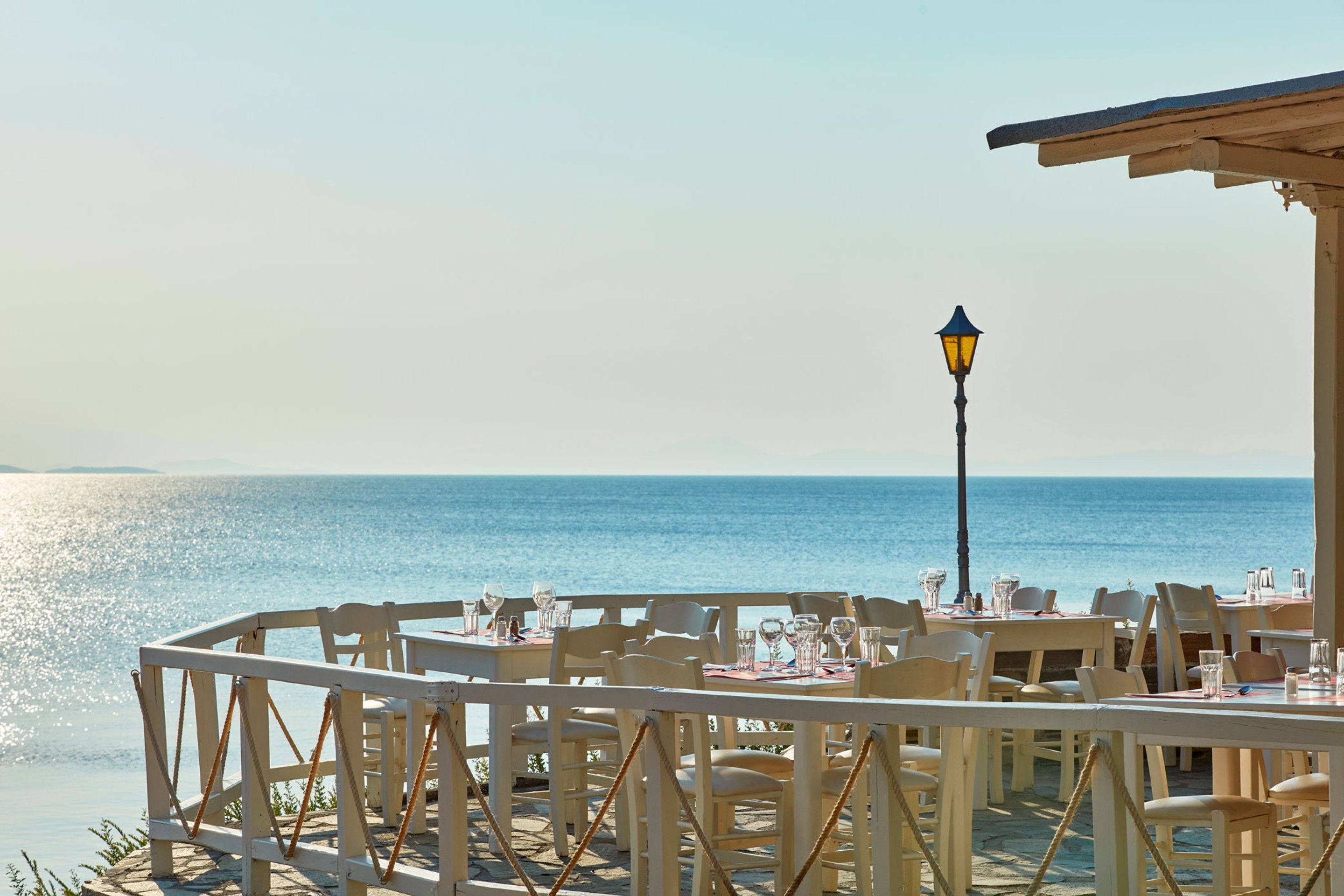 A seaside restaurant with tables and chairs set up for dining, overlooking the ocean.