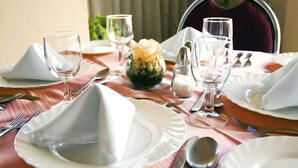 Una mesa de comedor dispuesta con platos blancos, cubiertos y cristalería.