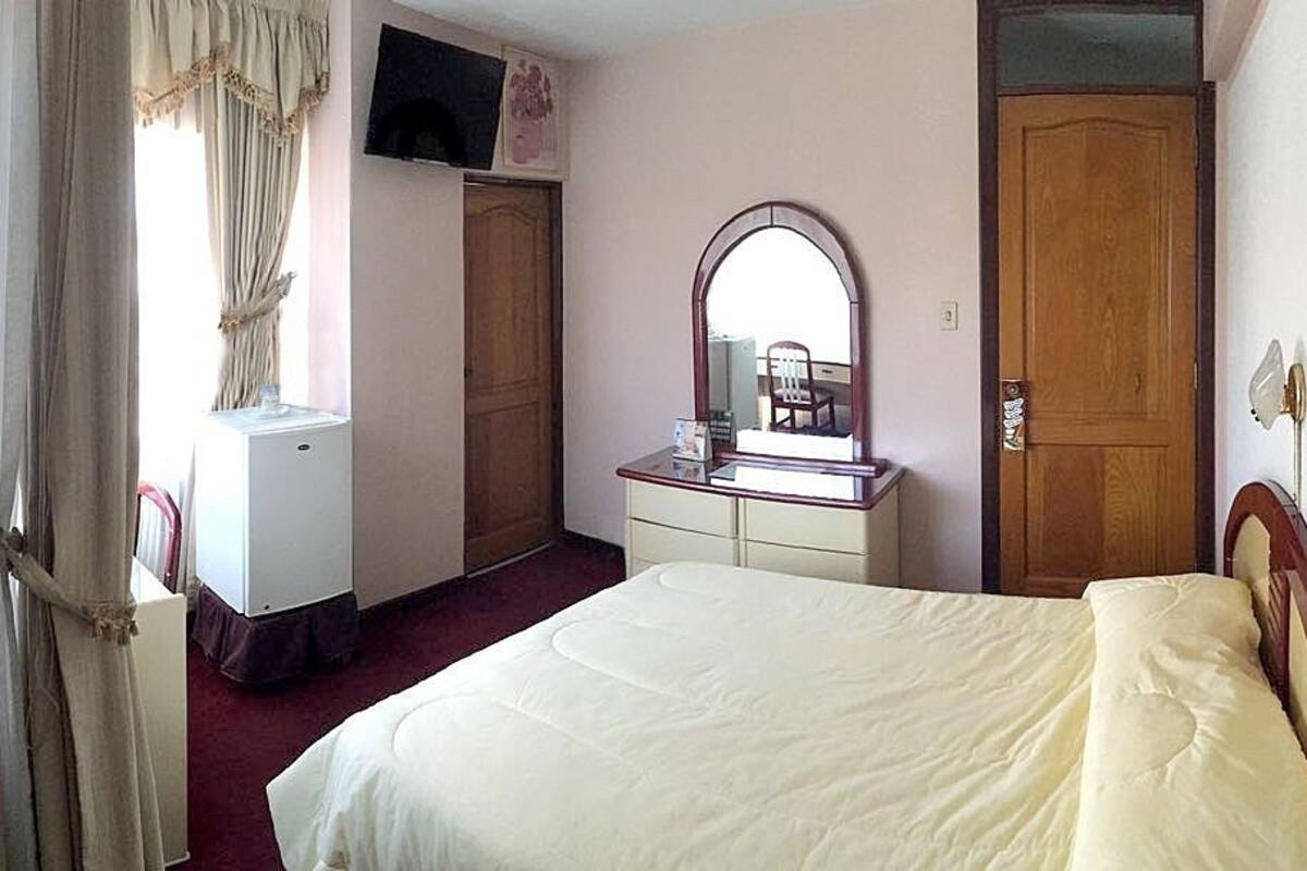 A bedroom with a bed, a dresser, a mirror, a television on the wall, and a wardrobe.