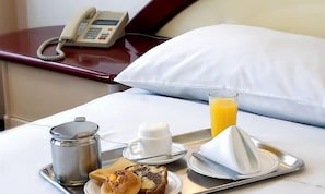 A hotel room with a bed, a bedside phone, a tray with breakfast items including toast, a muffin, a glass of orange juice, and a coffee pot. - Americana Hotel (Cochabamba)