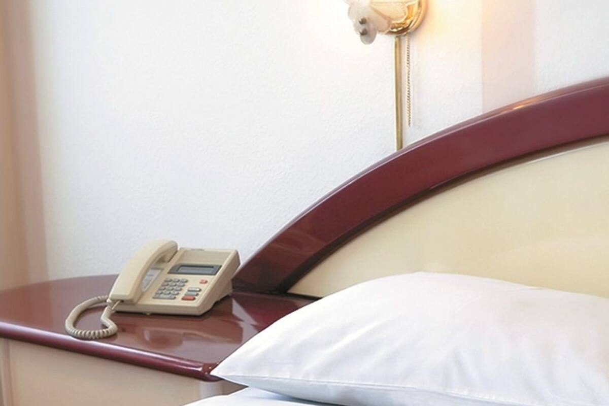 A hotel room with a bed, a bedside table with a telephone, and a wall-mounted light fixture.