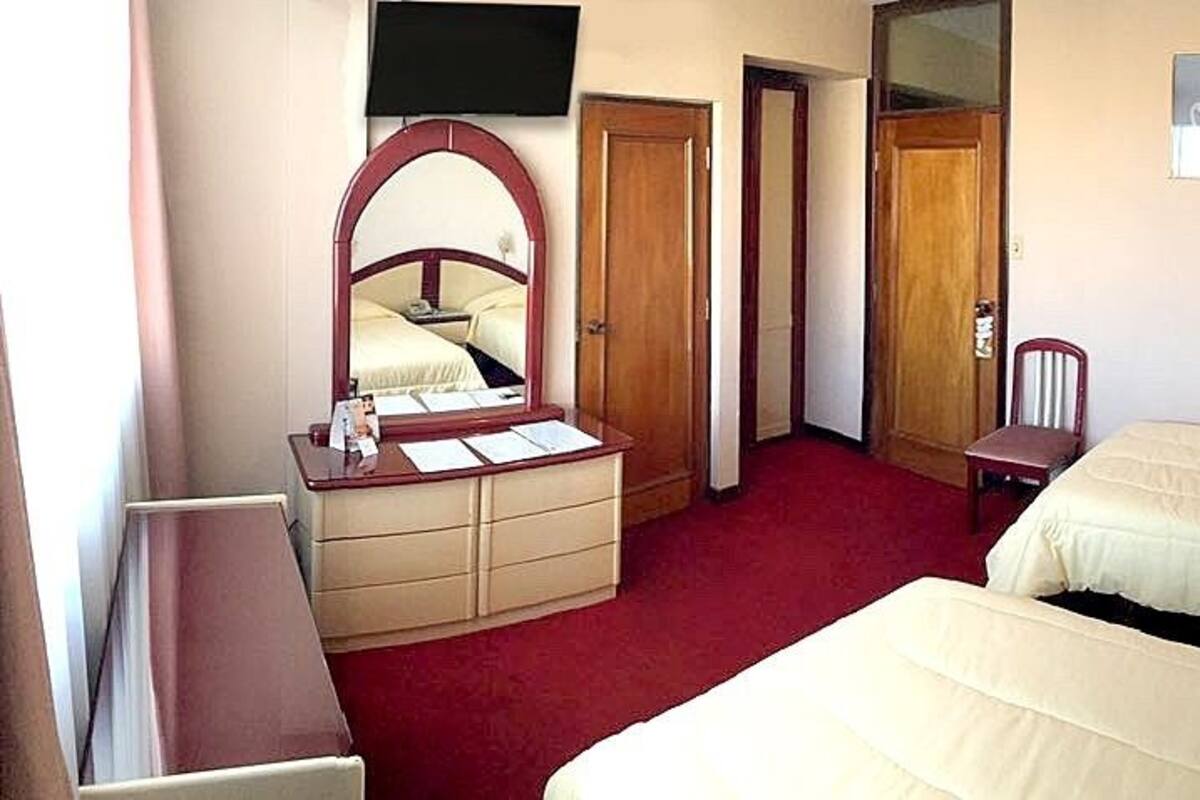 A hotel room with two beds, a dresser, a chair, a desk, and a television.