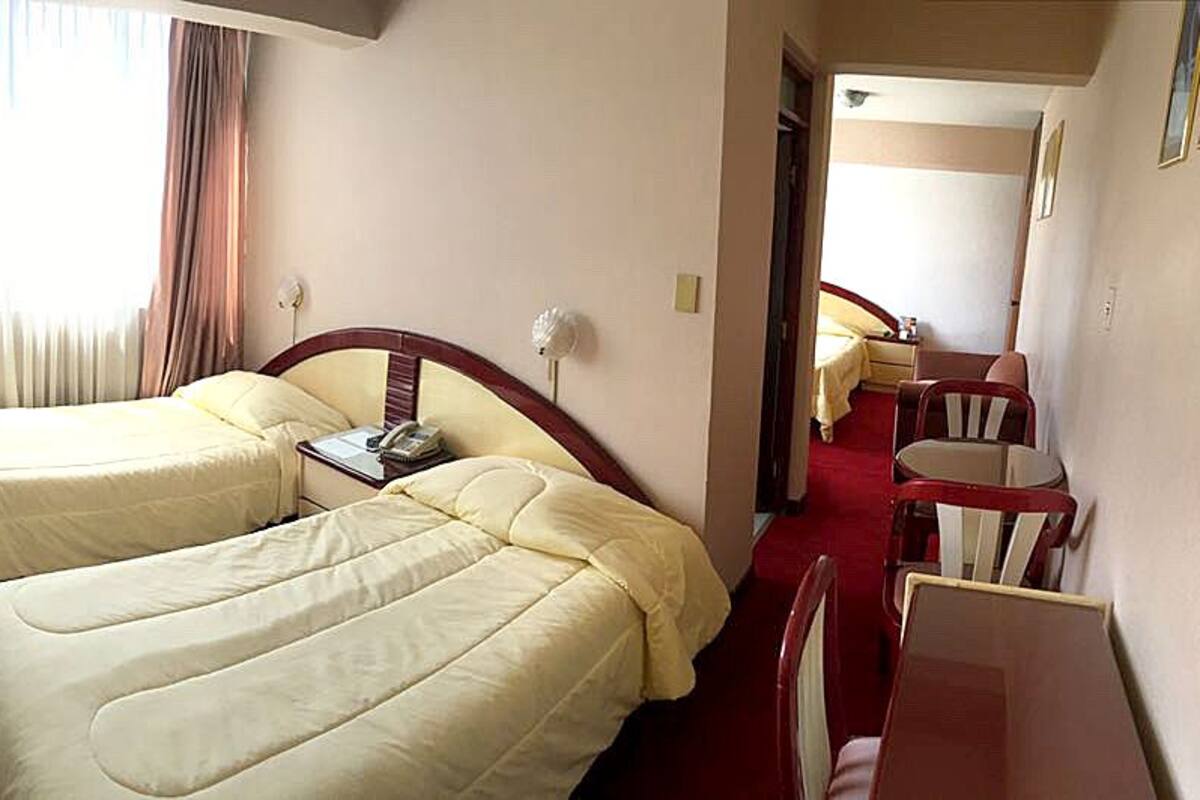 A hotel room with two beds, a desk, a chair, a telephone, and a window with curtains.