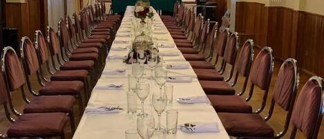 A long dining table set for a formal event, flanked by rows of chairs.