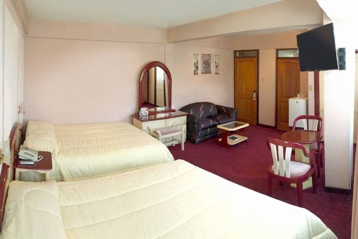A hotel room with two beds, a desk, a chair, a TV, and a wardrobe.