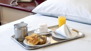 Habitación de hotel con cama, mesita de noche con teléfono, bandeja con artículos de desayuno y una lámpara fijada a la pared.