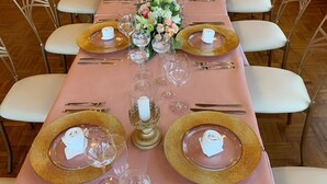 Una larga mesa de comedor dispuesta con platos de borde dorado, copas de cristal transparentes y servilletas blancas.