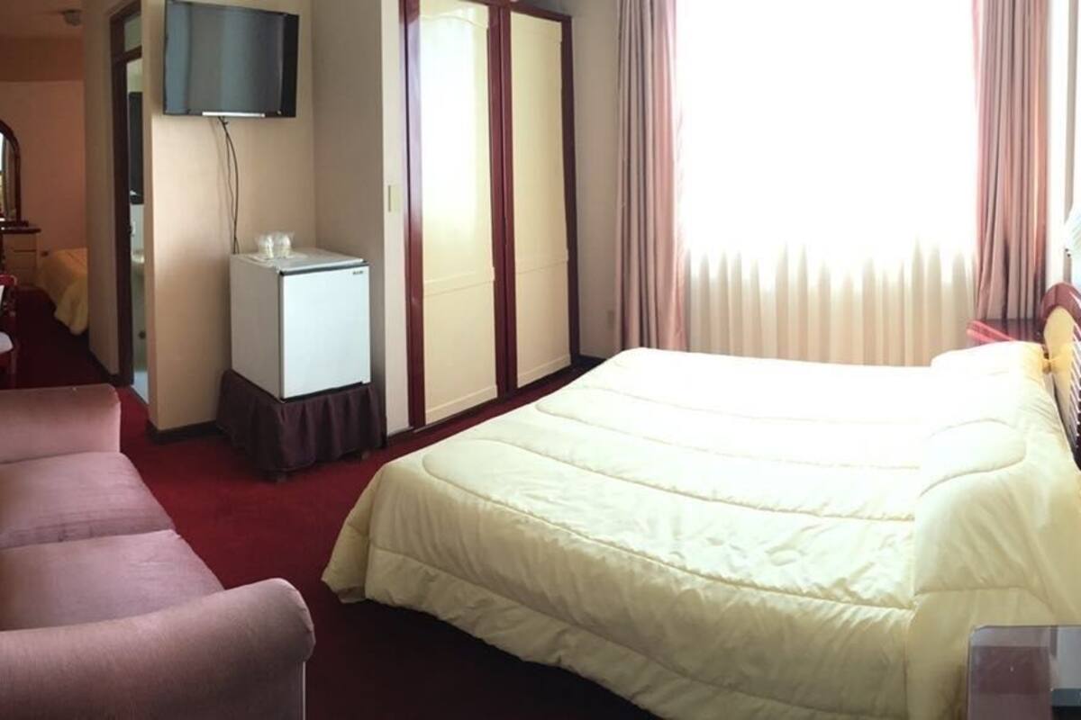 A hotel room with a bed, a desk, a chair, a television, and a wardrobe.
