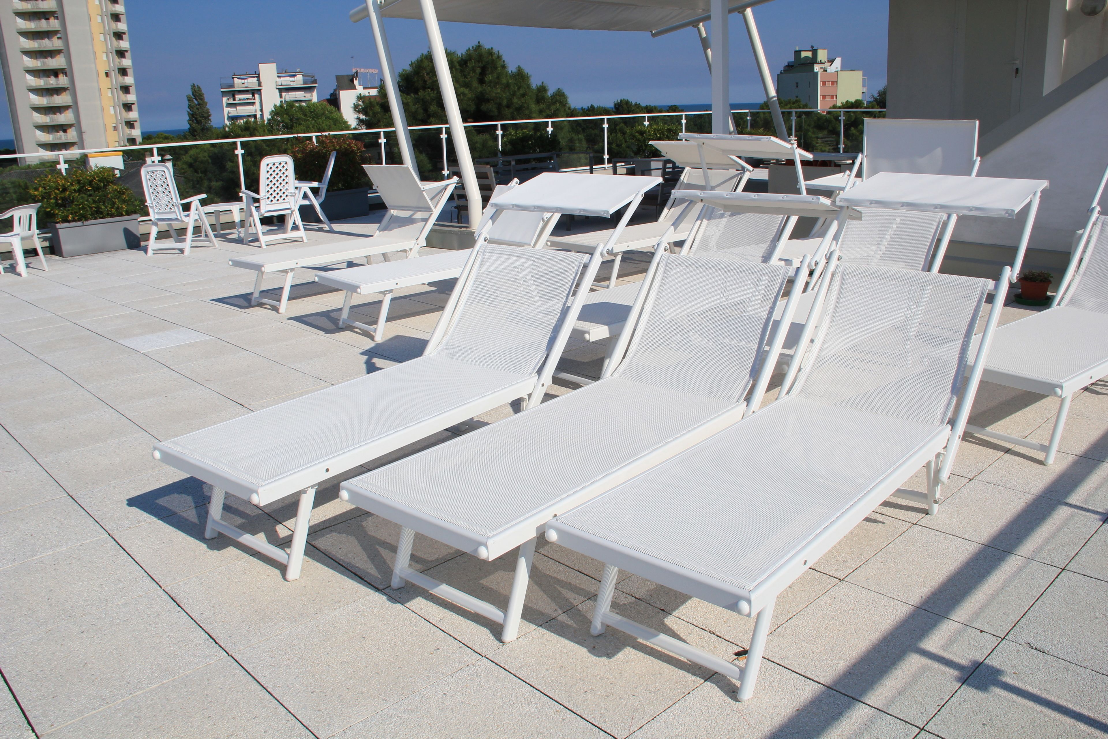 A rooftop lounge area with white lounge chairs and tables, a covered seating area, and a view of the cityscape.