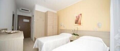 Une chambre d’hôtel avec deux lits, une armoire, un miroir et une petite table sur laquelle est posé un vase de fleurs.