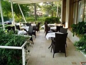 An outdoor patio area with tables and chairs, surrounded by greenery and a white railing.